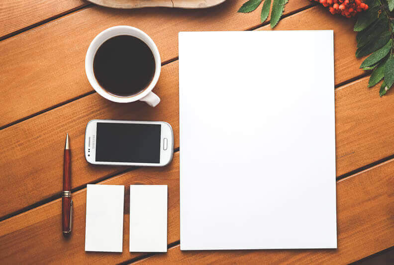 Mesa de trabalho com celular, caderno, caneta, xícara de café e notebook